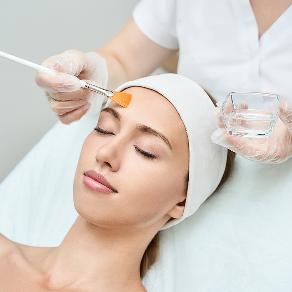 Young woman with eyes closed receiving skin care, chemical peel by esthetician.