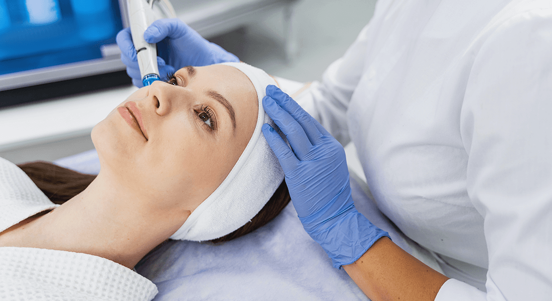 Woman lying down receiving hydra-dermabrasion treatment by professional esthetician.